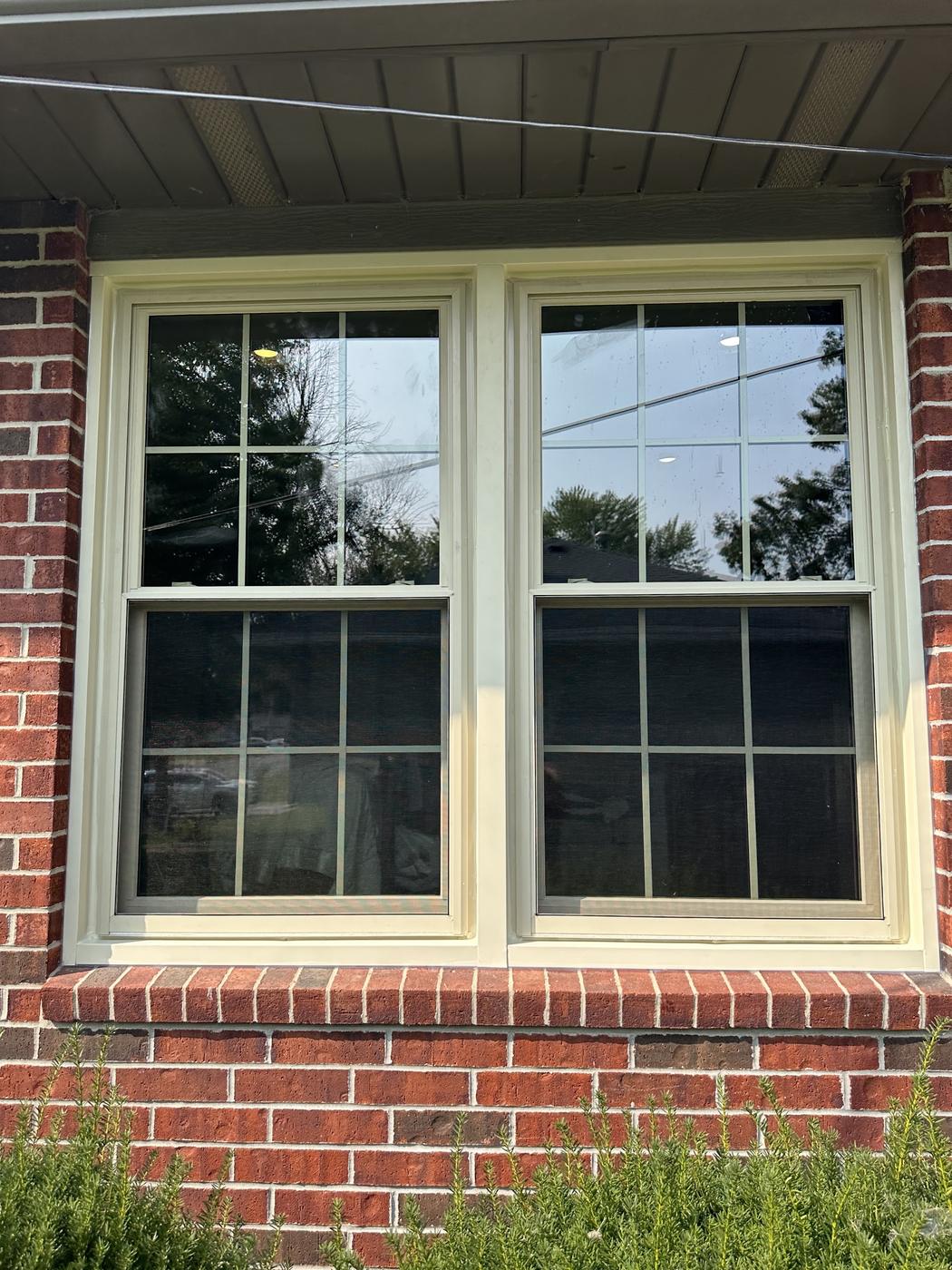A completed double-window install on a brick house, white grid-pane frames, close daylight shot