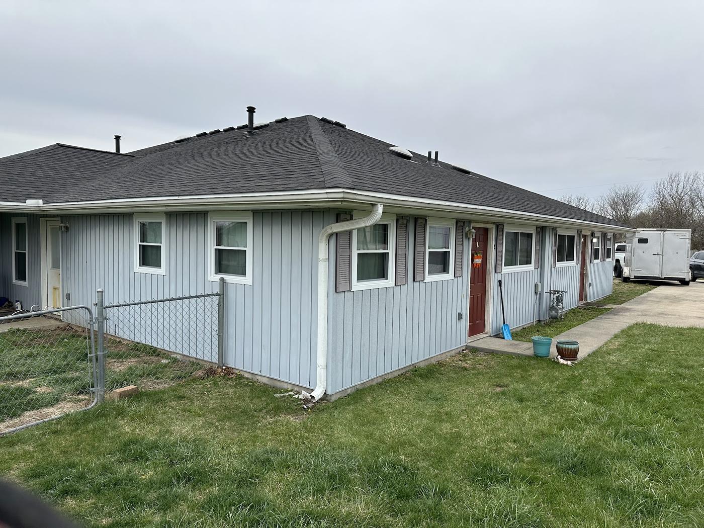 A multi-unit residential row with new white-framed windows and shutters across several units, a company trailer visible in the driveway