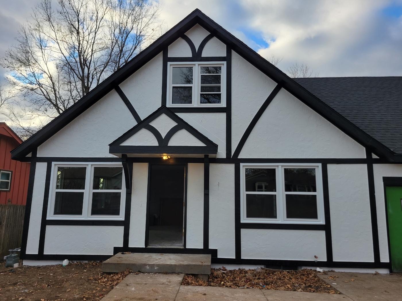 A black-and-white Tudor-style house with several completed window installs, full-house architectural shot